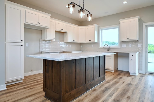 kitchen with white cabinetry, light wood-style floors, backsplash, and pendant lighting