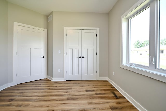 unfurnished bedroom with light wood-type flooring, visible vents, baseboards, and a closet