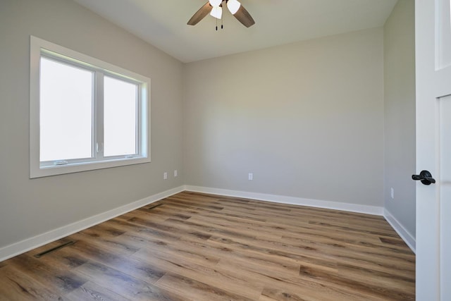 spare room featuring ceiling fan, visible vents, baseboards, and wood finished floors