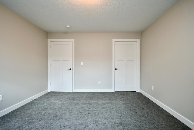 unfurnished bedroom featuring dark carpet, a textured ceiling, and baseboards