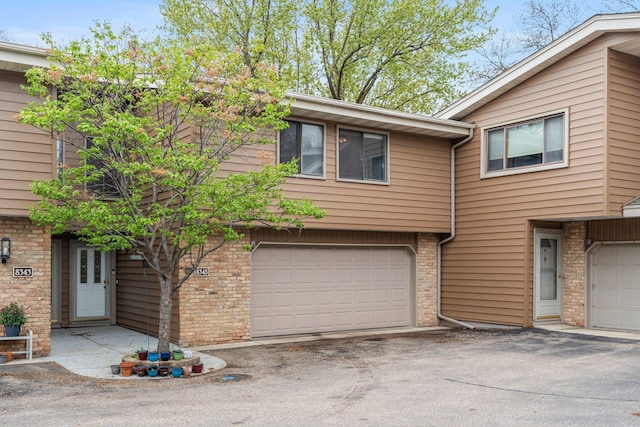 view of property with a garage, brick siding, and driveway