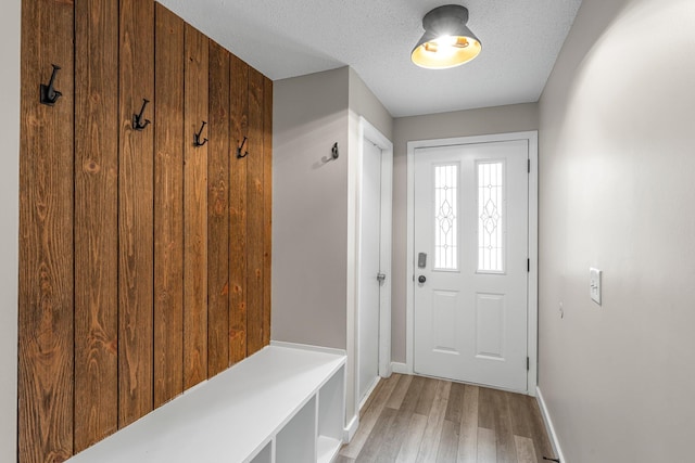 mudroom featuring baseboards, light wood finished floors, and a textured ceiling