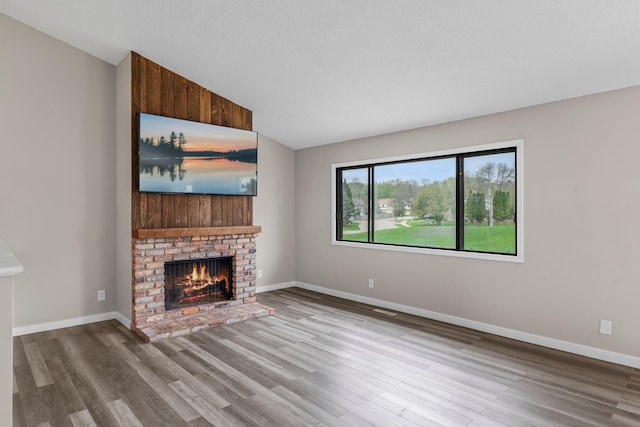 unfurnished living room with a fireplace, lofted ceiling, baseboards, and wood finished floors