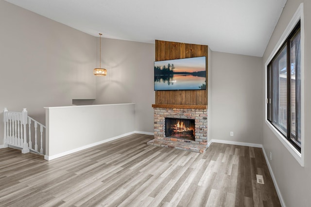 unfurnished living room with baseboards, wood finished floors, lofted ceiling, and a fireplace