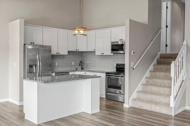 kitchen featuring light wood finished floors, stainless steel appliances, baseboards, and backsplash