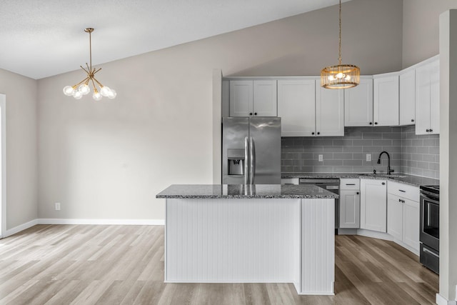 kitchen with an inviting chandelier, dark stone countertops, a sink, light wood-style floors, and appliances with stainless steel finishes