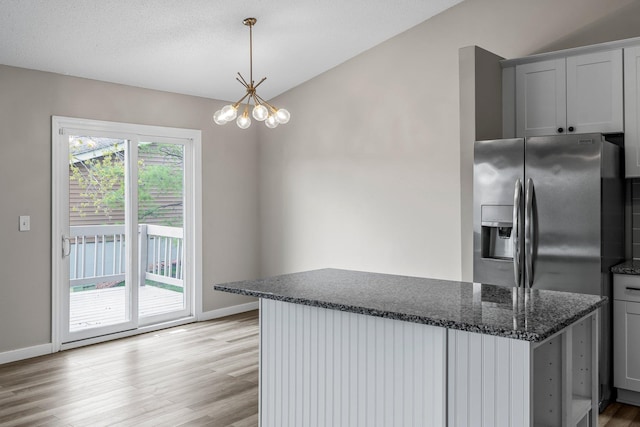 kitchen featuring a notable chandelier, baseboards, stainless steel fridge with ice dispenser, dark stone countertops, and light wood-type flooring