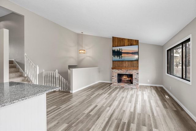 unfurnished living room with baseboards, a brick fireplace, light wood-type flooring, and high vaulted ceiling