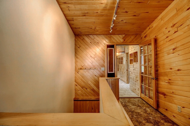 hall with track lighting, lofted ceiling, wooden walls, wood ceiling, and an upstairs landing