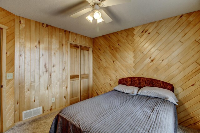 carpeted bedroom with visible vents, wood walls, and a ceiling fan