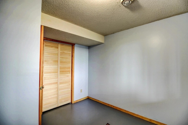 empty room featuring a textured ceiling, concrete floors, and baseboards