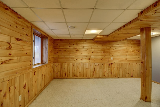 interior space with baseboards, light floors, a drop ceiling, and wooden walls