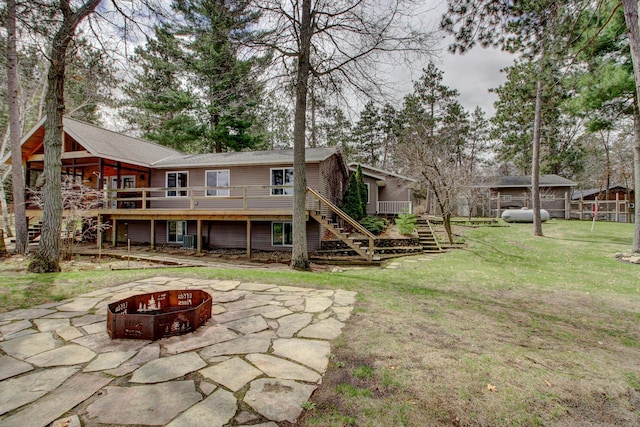 rear view of property with a lawn, a wooden deck, an outdoor fire pit, a patio, and stairs