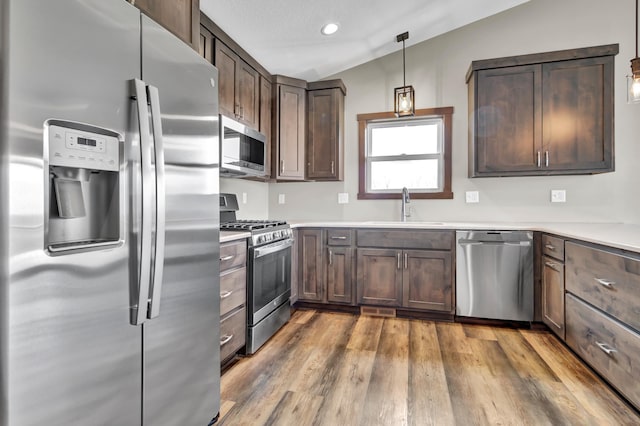 kitchen with wood finished floors, lofted ceiling, a sink, light countertops, and appliances with stainless steel finishes