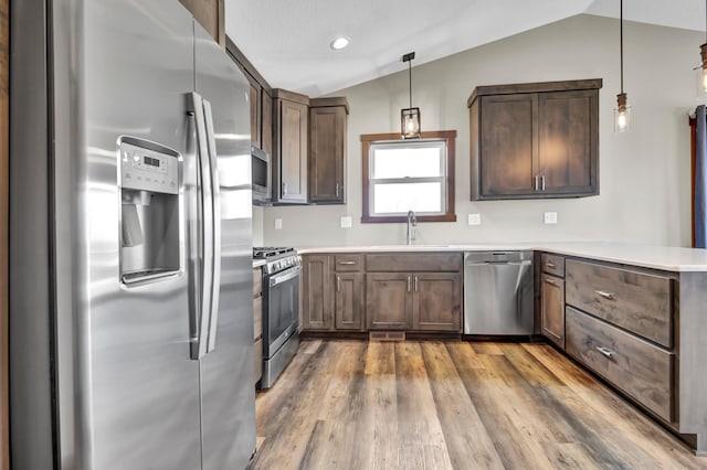 kitchen featuring wood finished floors, a peninsula, a sink, vaulted ceiling, and appliances with stainless steel finishes