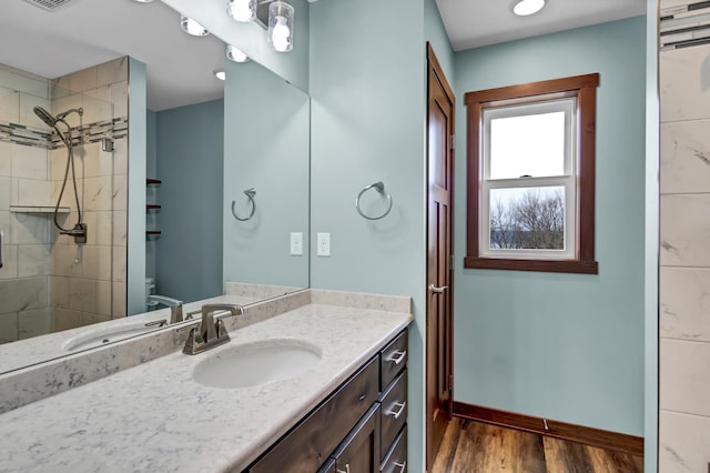 bathroom with visible vents, wood finished floors, tiled shower, baseboards, and vanity