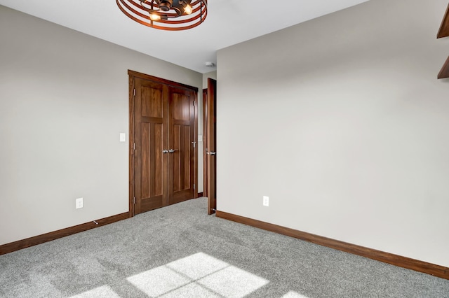 carpeted spare room featuring baseboards and an inviting chandelier