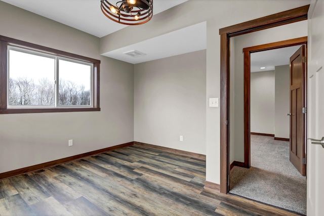 unfurnished room with visible vents, baseboards, an inviting chandelier, and wood finished floors