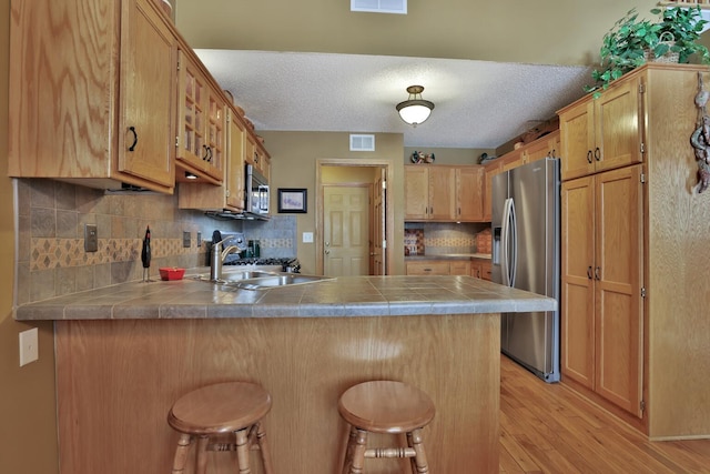 29561 Mentzer Ct, Lindstrom, MN 55045 - kitchen featuring appliances with stainless steel finishes, a peninsula, a breakfast bar area, light wood-type flooring, and a textured ceiling