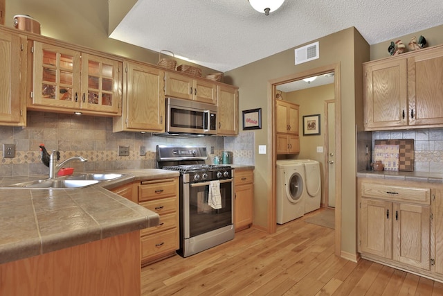 29561 Mentzer Ct, Lindstrom, MN 55045 - kitchen featuring stainless steel appliances, washing machine and clothes dryer, a sink, light wood-type flooring, and glass insert cabinets