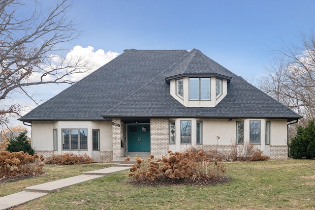 view of front facade featuring brick siding, stucco siding, a front yard, and roof with shingles