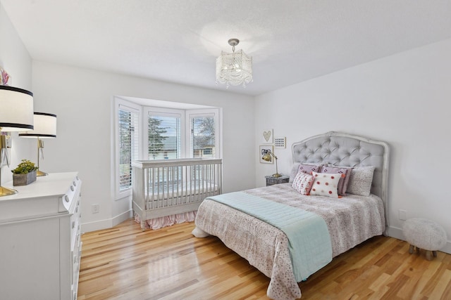 bedroom with a notable chandelier, light wood-style flooring, and baseboards