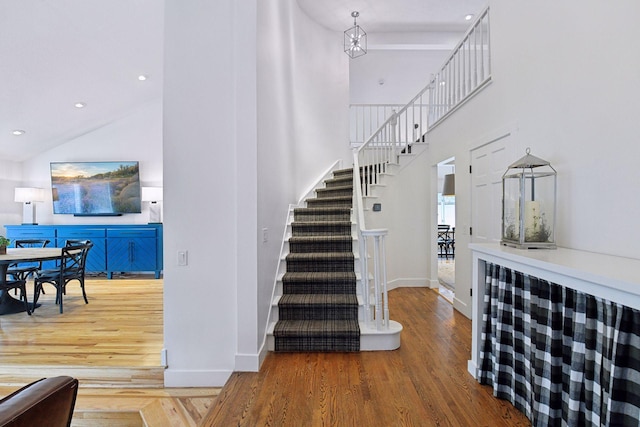 stairway with baseboards, wood finished floors, and a towering ceiling