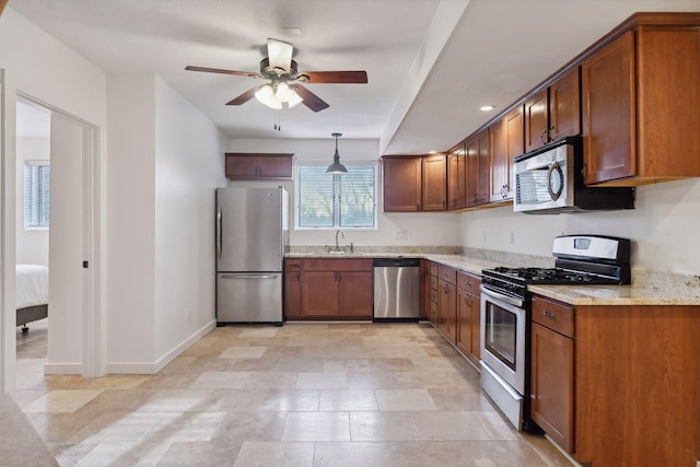 kitchen featuring light stone countertops, a ceiling fan, baseboards, a sink, and appliances with stainless steel finishes