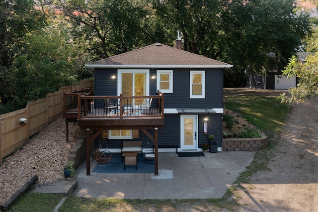 rear view of property featuring a wooden deck, fence, a patio, roof with shingles, and a chimney