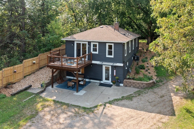 back of property featuring fence, a deck, a patio, roof with shingles, and a chimney