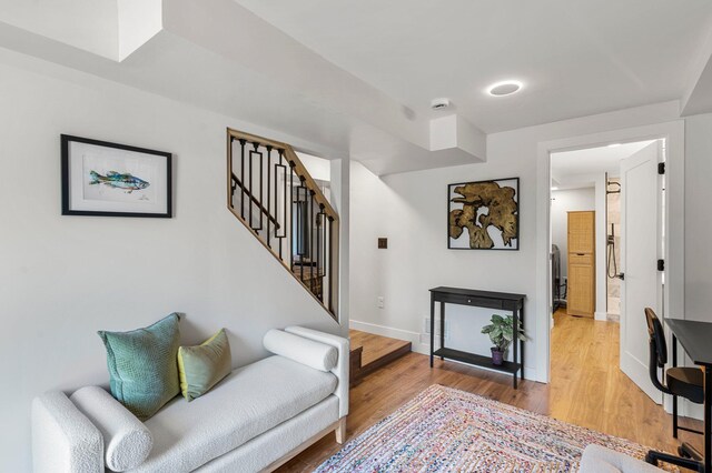 living area featuring baseboards, light wood-style flooring, and stairway