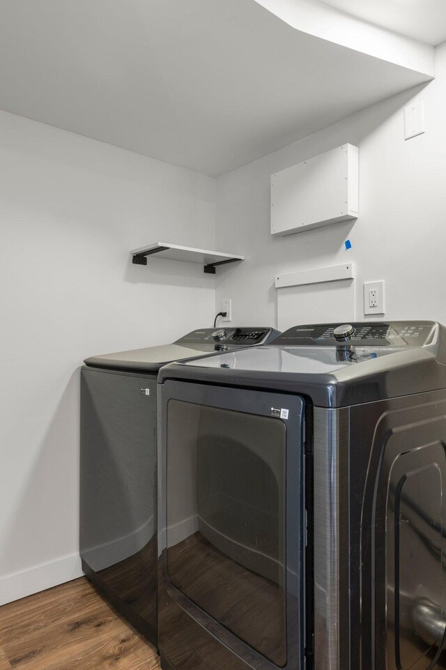 clothes washing area featuring baseboards, laundry area, wood finished floors, and washer and clothes dryer