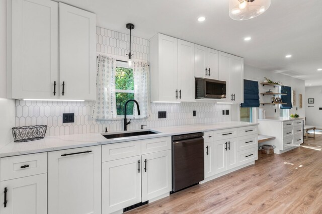 kitchen with black dishwasher, stainless steel microwave, white cabinets, a sink, and light wood-style flooring