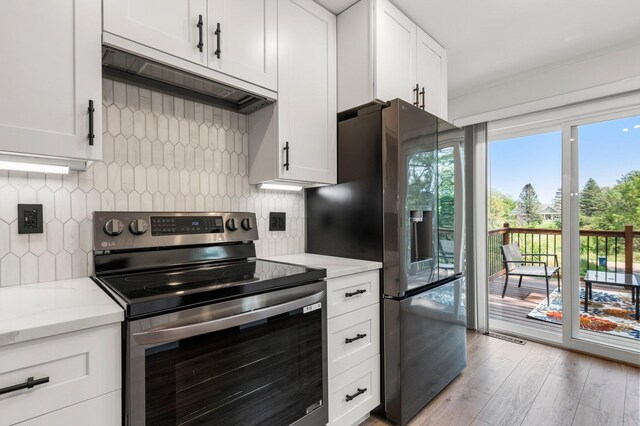 kitchen featuring light stone countertops, light wood-style floors, stainless steel appliances, backsplash, and under cabinet range hood