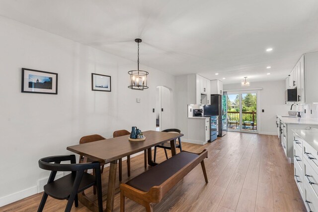 dining space with baseboards, arched walkways, light wood-style flooring, and recessed lighting