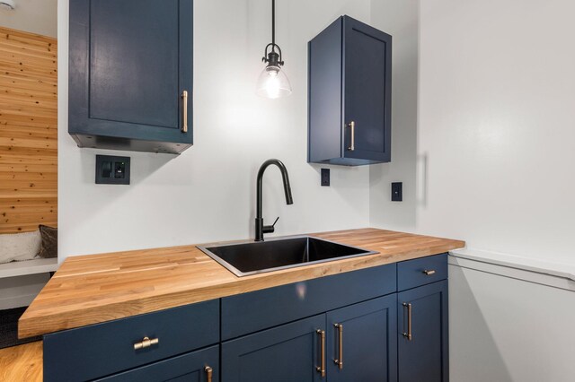 kitchen featuring decorative light fixtures, blue cabinetry, butcher block countertops, and a sink