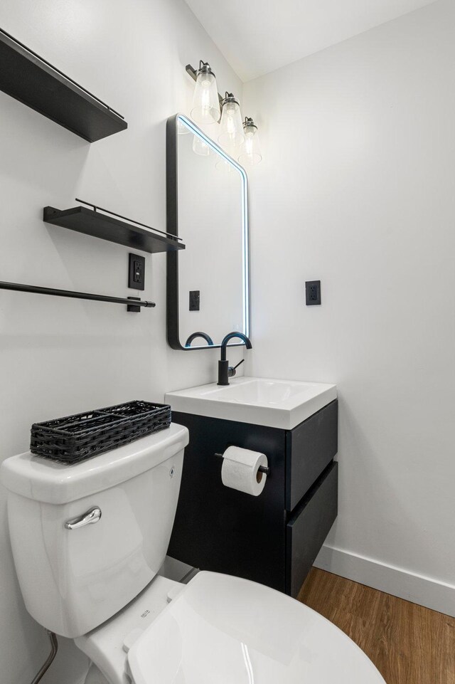 half bathroom featuring baseboards, wood finished floors, toilet, and vanity