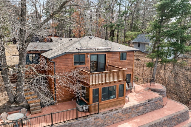 rear view of property featuring a wooden deck, a patio area, and roof with shingles