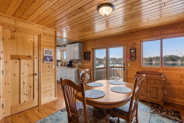 dining room with light wood finished floors, wooden ceiling, wooden walls, and a water view