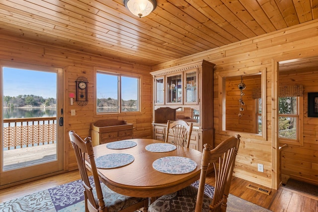 dining space with wooden ceiling, light wood-style floors, and wooden walls