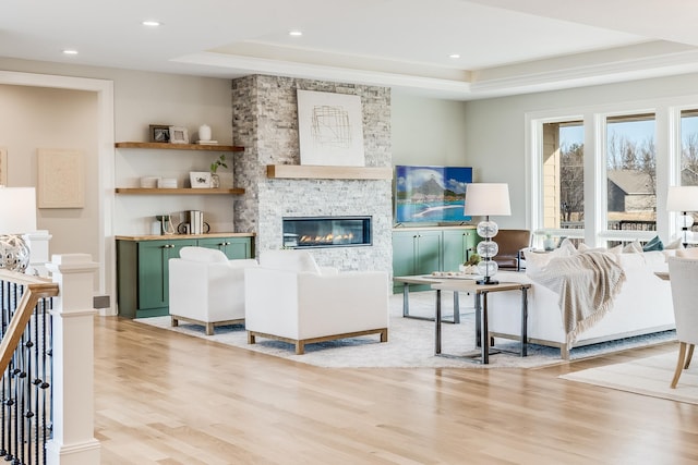 living room with recessed lighting, a stone fireplace, a tray ceiling, and wood finished floors