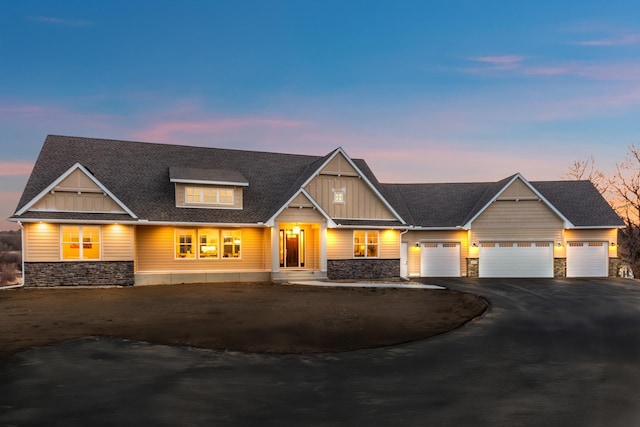 view of front facade with aphalt driveway, a shingled roof, an attached garage, board and batten siding, and stone siding