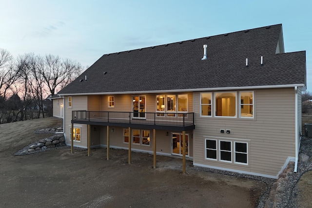 back of house at dusk with roof with shingles and a deck