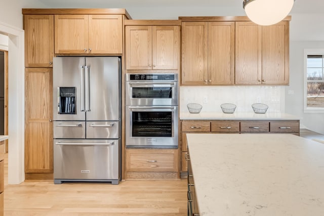 kitchen with light stone counters, light wood finished floors, appliances with stainless steel finishes, and decorative backsplash