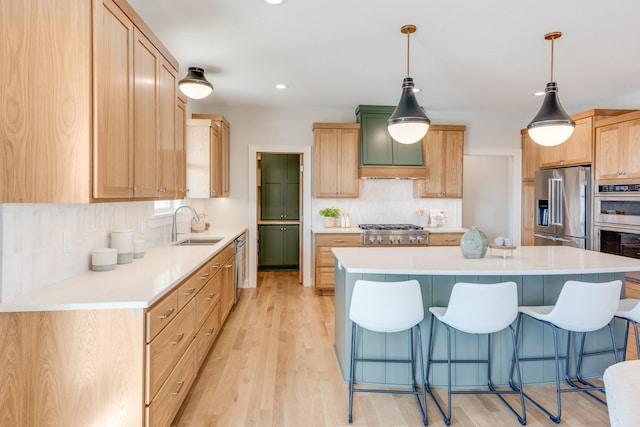 kitchen with a sink, light wood-style floors, a kitchen bar, backsplash, and appliances with stainless steel finishes