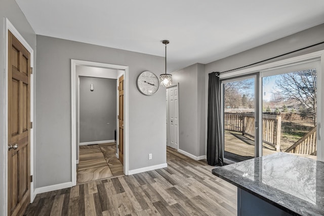 unfurnished dining area featuring baseboards, wood finished floors, and an inviting chandelier