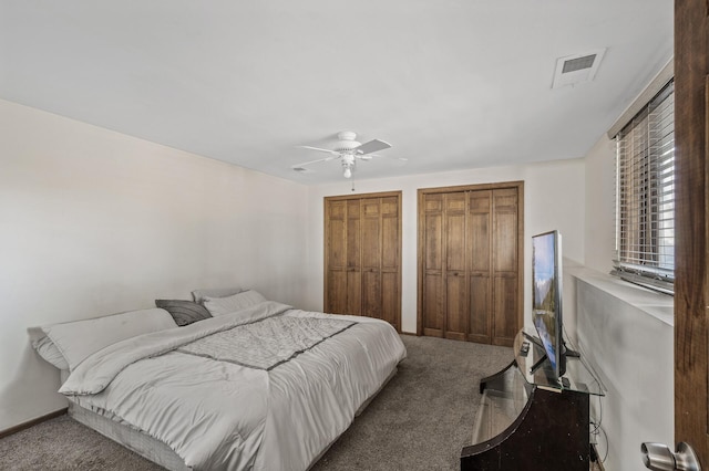 bedroom with carpet flooring, a ceiling fan, visible vents, and two closets
