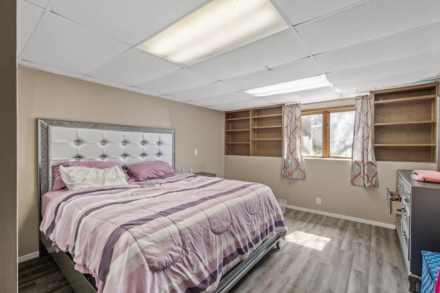 bedroom featuring a paneled ceiling, baseboards, and wood finished floors