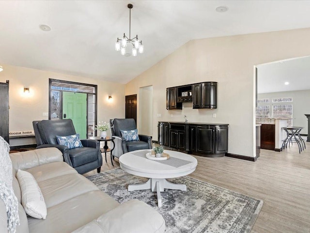 living area featuring lofted ceiling, a notable chandelier, light wood finished floors, and baseboards