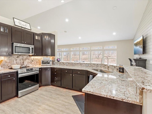 kitchen featuring a sink, tasteful backsplash, light wood-type flooring, vaulted ceiling, and appliances with stainless steel finishes